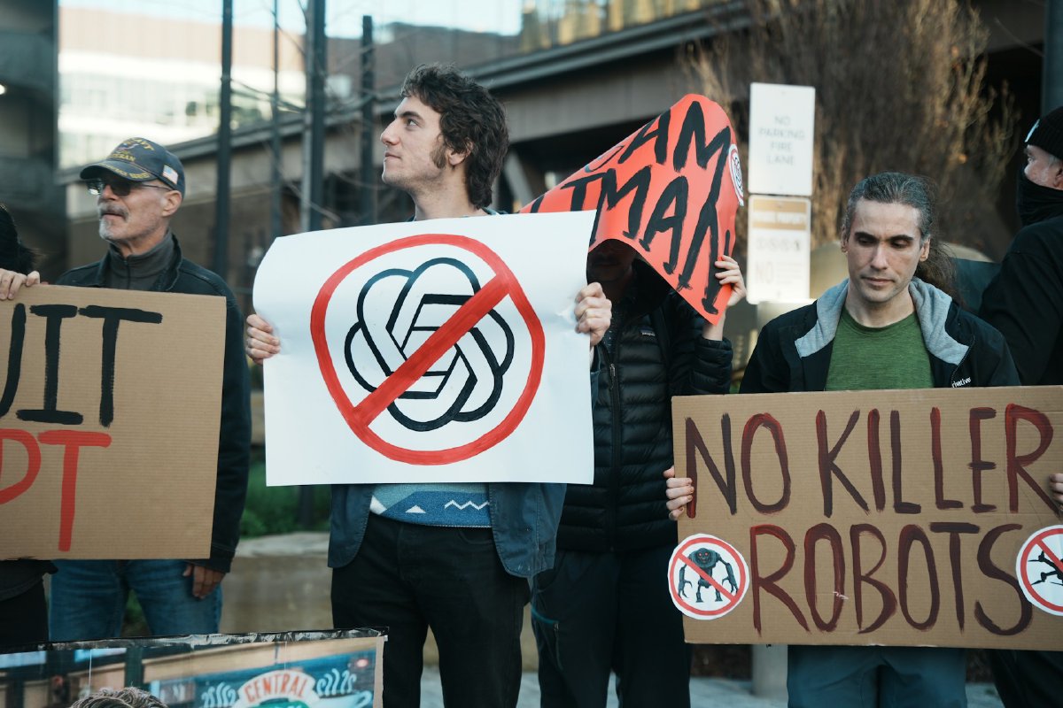 Protesters holding signs reading 'No Killer Robots' and a crossed-out OpenAI logo at a street demonstration against AI